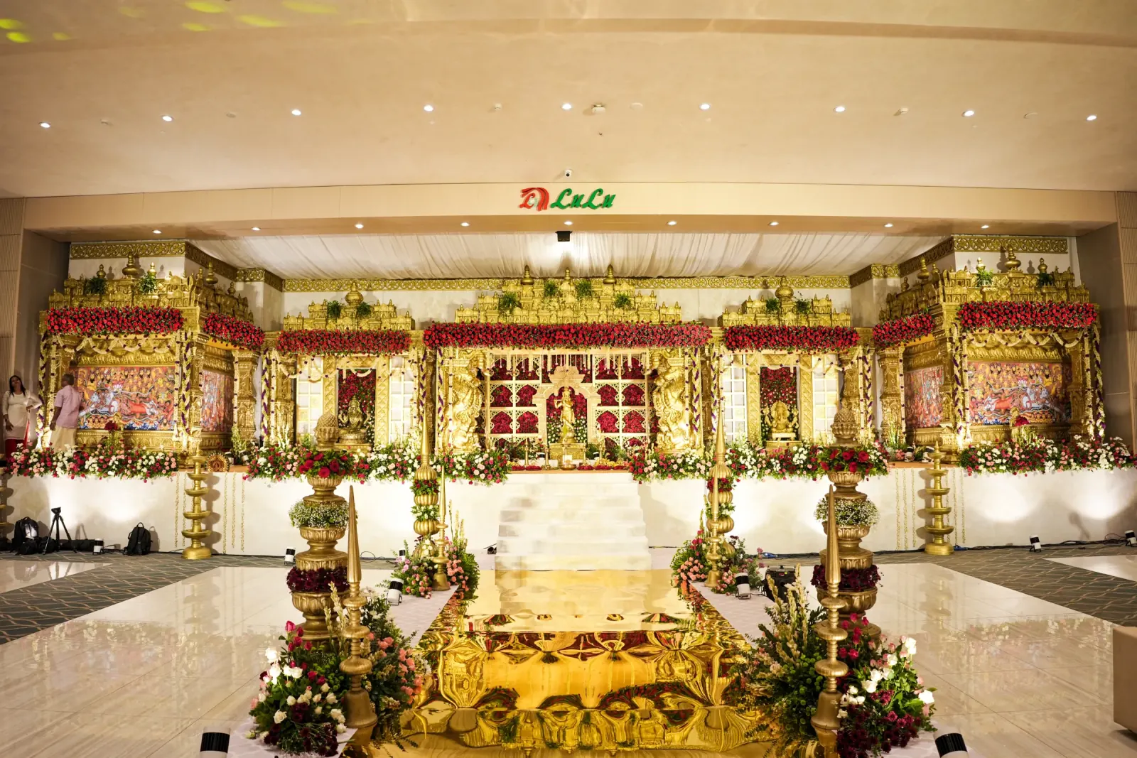 Grand gold temple wedding stage with red roses and ceremonial aisle