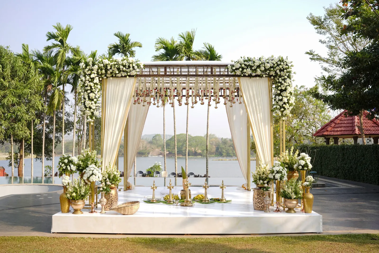 Lakefront white floral mandap with ivory drapes and brass lamps