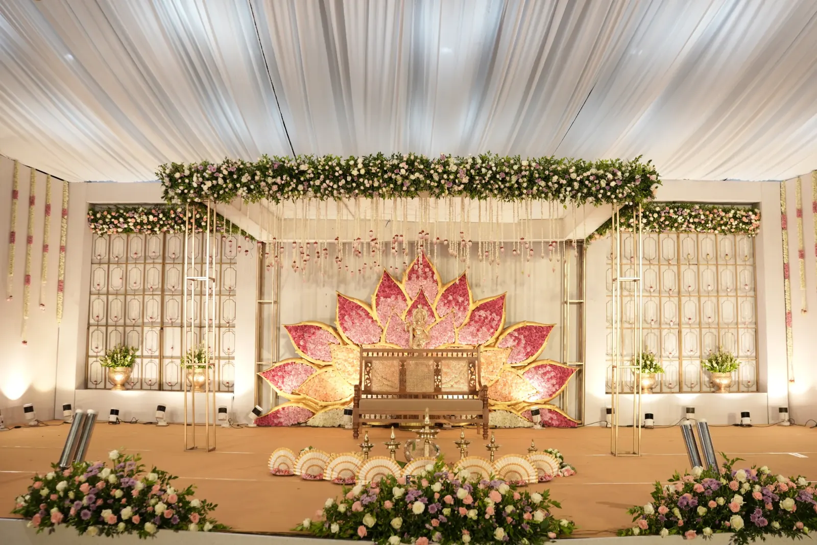 Pink lotus floral wedding stage with ivory draping and brass décor