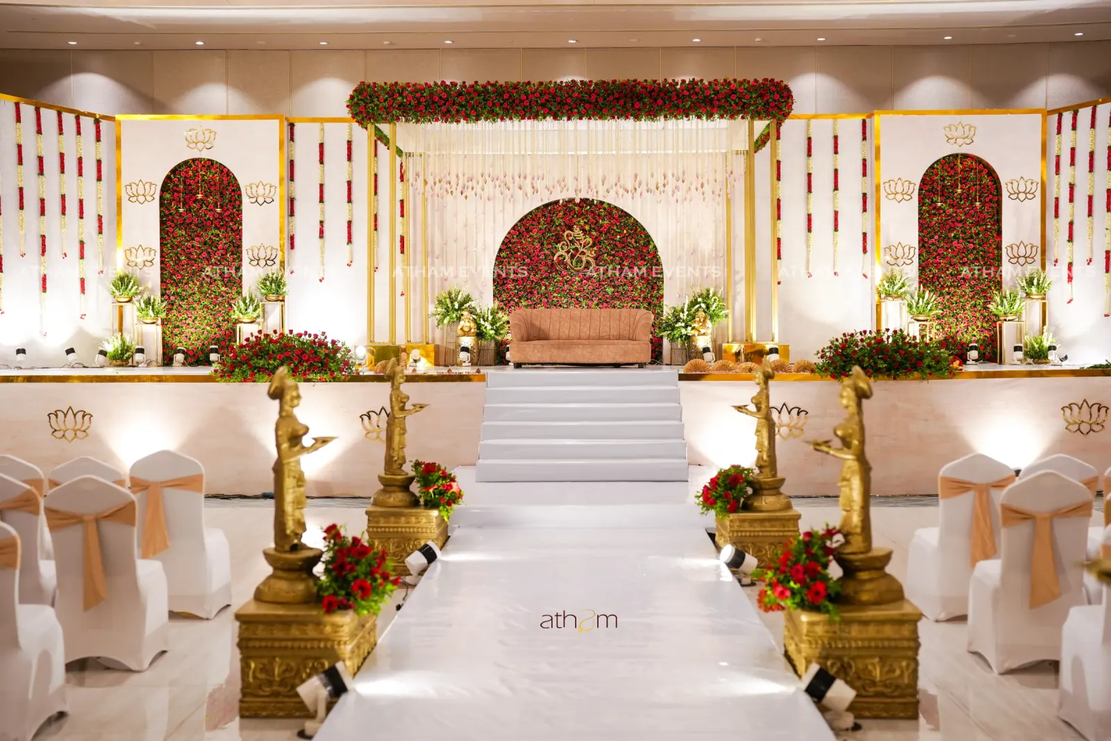 Red rose Ganesh wedding stage with gold accents and ceremonial aisle